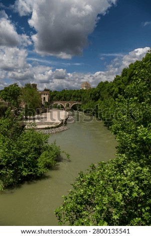 The green trees lining the River Tiber and Fabricio bridge in Rome Italy on a sunny day