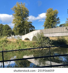 Green trees, plants, old stone walls, and a black metal railing next to a river with a wooden bridge in summer in Cork, Ireland - Powered by Shutterstock