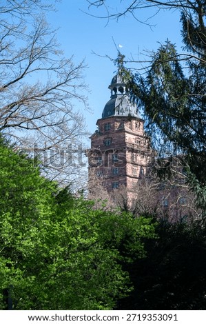 Green trees stand in front of a tower of Johannisburg Castle in Aschaffenburg , Germany, against a blue sky