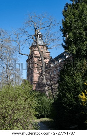 Green trees stand in front of a tower of Johannisburg Castle in Aschaffenburg , Germany, against a blue sky
