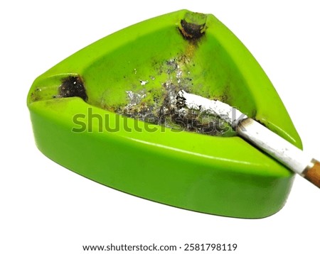 A green triangular ashtray with a lit cigarette and ashes isolated on white background. Ideal for smoking, health, addiction, and lifestyle-related content.