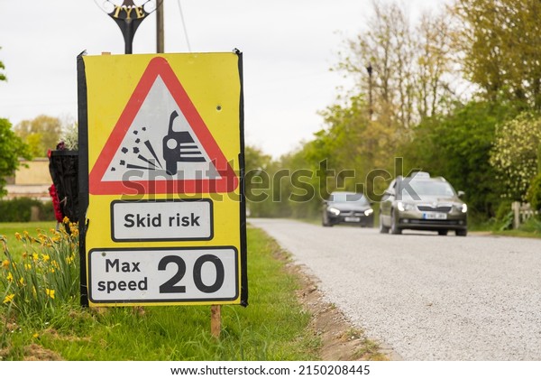Green Tye, Much Hadham, Hertfordshire. UK. April\
27th 2022. Cars passing a sign warning drivers of a skid risk on a\
newly resurfaced road.