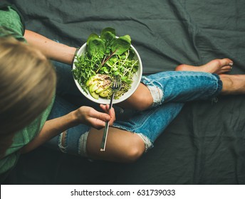 Green vegan breakfast meal in bowl with spinach, arugula, avocado, seeds and sprouts. Girl in jeans holding fork with knees and hands visible, top view. Clean eating, detox, vegetarian food concept - Shutterstock ID 631739033