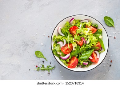 Ensalada vegetariana de hojas verdes mezcladas y verduras. Vista superior sobre la mesa de piedra gris.