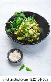 Green Vegetarian Fusilli Pasta With Zucchini Pesto And Herbs On A White Marble Background In A Black Bowl. Healthy And Economical Recipes For The Whole Family, Italian Pasta, Front View