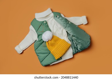 Green vest jackets with warm sweater on orange background. Stylish childrens outerwear. Winter fashion outfit 