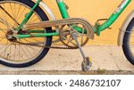 Green vintage old  bicycle with rust and worn paint is parked against yellow wall. Bicycle