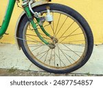 Green vintage old bicycle with rust and worn paint is parked against yellow wall. Bicycle