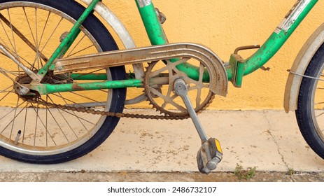 Green vintage old  bicycle with rust and worn paint is parked against yellow wall. Bicycle's frame and chain are both slightly rusted - Powered by Shutterstock