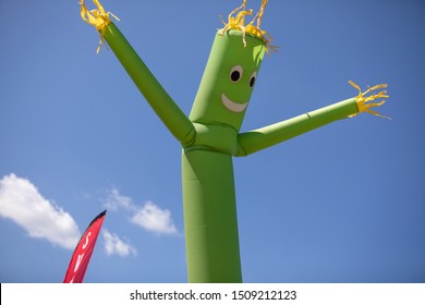 A Green Wacky Waving Inflatable Arm Flailing Tube Man With Yellow Hair Against A Bright Blue Sky With A Single Cloud.