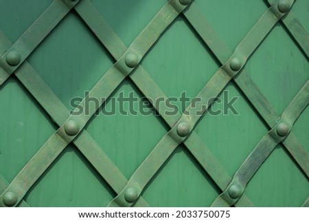 Green wall decorated with a diamond-shaped pattern of metal plates and buttons