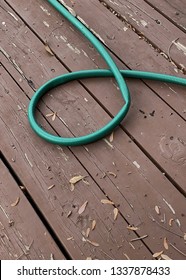 Green Water Hose Curled On A Wooden Deck With A Possible Kink