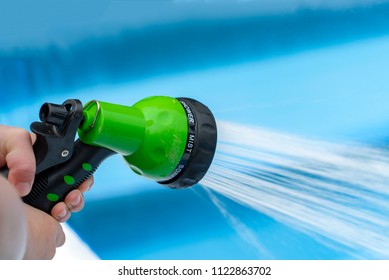 Green Water Jet Adjustable Sprinkler Being Angled In The Direction Of An Outdoor Paddling Pool.