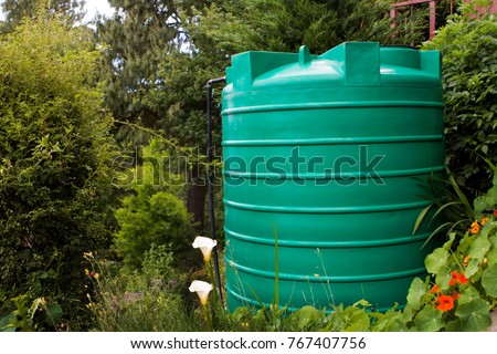 Green water tank in a garden setting with flowers in the foreground