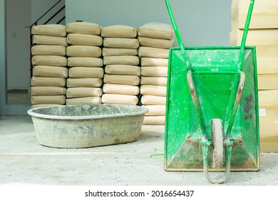 Green wheelbarrow and mortar mixing tank Pile of Cement in brown bags in a construction site with gray wall background - Shutterstock ID 2016654437