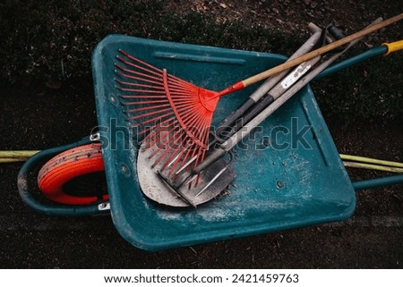 Green wheelbarrow with rakes and shovels top view. Garden tools, equipment on a backyard. Working hard on orchard, greenhouse. Cart for works outdoors