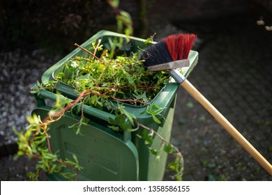 Green Wheelie Bin / Garden Waste Container And Broom Filled With Fruit And Vegetable Waste, Garden Waste, Organic Waste For Composting And Fermentation. Recycling Garbage For A Better Environment.