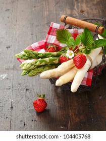Green and white Asparagus and Strawberries in a wire basket on wooden background