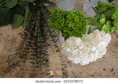 Green and white hydrangeas, along with eucalyptus stems and fresh greenery, arranged on a textured countertop, creating a natural, rustic setting for floral arrangement and bouquet preparation. - Powered by Shutterstock