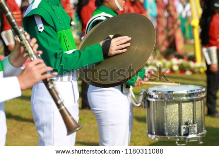 Green and white uniform cymbals player in marching band with drumer and clarinet player.