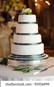 Green And White Wedding Cake At Reception In Barn.