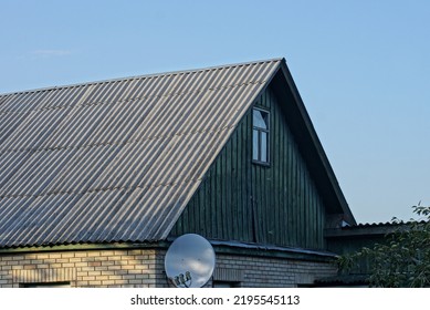 Green Wooden Attic With An Small Window Of A Rural House Under A Gray Slate Roof Against A Blue Sky