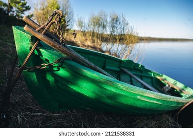 A green wooden boat with green The rowboat is moored with a rope. There's a rope around the bow of the boat