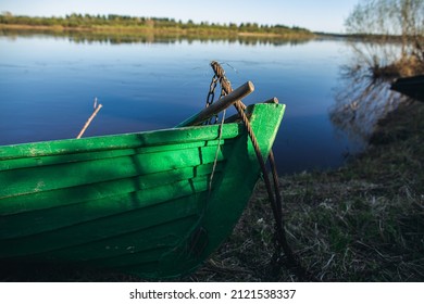 A green wooden boat with green The rowboat is moored with a rope. There's a rope around the bow of the boat