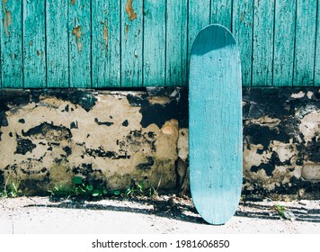 Green Wooden Skateboard On Deteriorated Wall On A Sunny Day. Skateboarding Background, Street Extreme Sport.