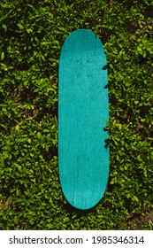 Green Wooden Skateboard On Grass Outdoors On A Sunny Day. Skateboarding Background, Street Extreme Sport. Summer Backdrop