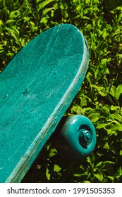 Green Wooden Skateboard On Grass Outdoors On A Sunny Day. Skateboarding Background, Street Extreme Sport.