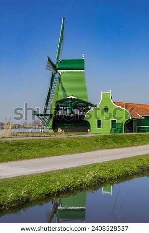 Green wooden windmill reflected in the canal of Zaanse Schans, Netherlands