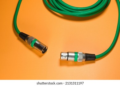 Green XLR microphone cable with metal jack on orange background isolated