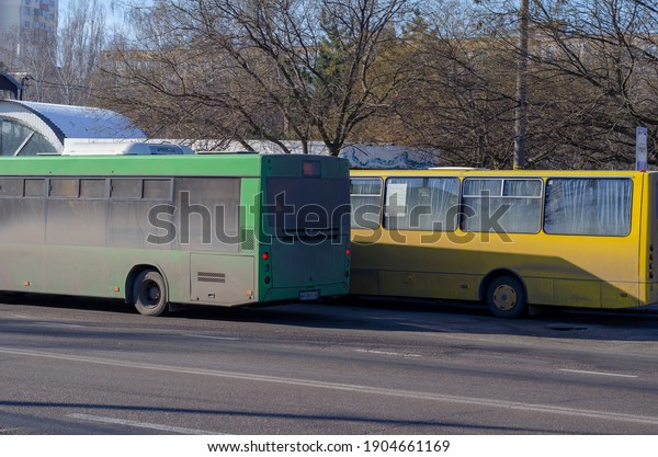 The green and yellow buses are at the bus stop. Two\
dirty buses at the passenger boarding and drop-off point: Nikolaev,\
Ukraine - January 21