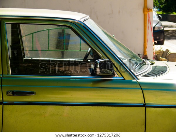 Green and\
yellow car side view. Transparent windows of car. Parked car\
closeup photo. Travel by transport. Empty driver seat. Simple\
vintage car. Automobile with simple design.\
