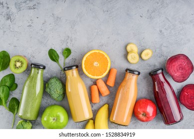 Green, Yellow, Orange And Red Smoothie In Glass Bottles With Fruits And Vegetables On Grey Background, Top View