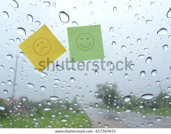 Green and yellow\
paper with happy and sad faces on the windshield with rain drop\
background outside.          \
