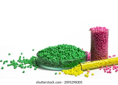 Green, yellow and pink granules of polypropylene or polyamide on a white background. Plastics and polymers industry. Copy space. Glass petri dish, flask, volumetric glassware, test tube.