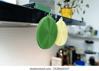 Green and yellow silicone dish scrubbers hang on a kitchen range hood, adding a pop of color and functionality to the cooking space - Powered by Shutterstock