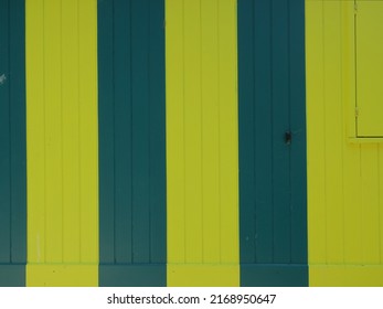 a green and yellow striped wooden cabin with a closed shutter