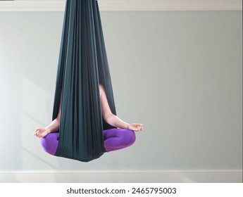 A green yoga hammock. An adult woman practices various inversion poses - anti-gravity poses - in a bright, well-lit studio. The picture was taken in close-up, without a face, there is a place for text - Powered by Shutterstock