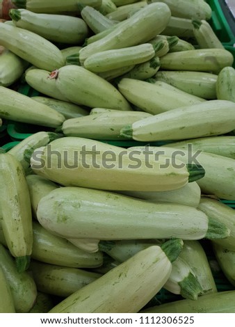 Green zucchini; Elongated green vegetable; Fresh picked green courgette offered at farmer's market; Summer squash