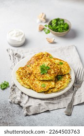 Green zucchini fritters, vegetarian zucchini pancakes with fresh herbs and garlic, served with cream sauce on white background, selective focus