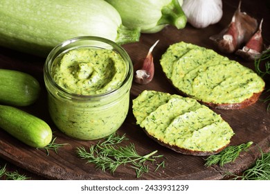 Green zucchini spread in a glass jar with whole wheat bread sandwiches on rustic dark background, healthy summer vegetarian food concept - Powered by Shutterstock