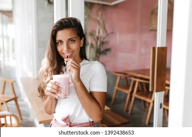 Green-eyed smiling woman in white T-shirt drinking milkshake sitting in cafe - Powered by Shutterstock