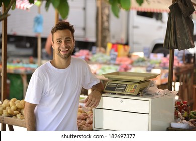 Greengrocer Owner Of A Small Business At An Open Street Market, Selling Organic Fruits And Vegetables.