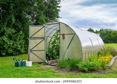 Greenhouse. A garden greenhouse in a farmer's garden. Watering cans and buckets near the greenhouse. Plastic greenhouse. Latvian: siltumnīca