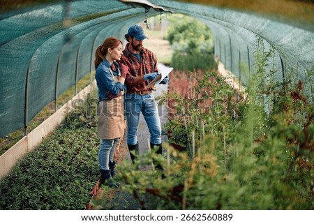 Greenhouse workers cooperating while going through paperwork.  Copy space. 