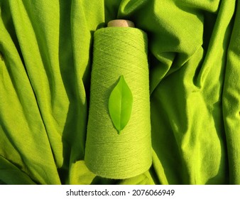 GreenSustainable Fashion:  Leaf on a green yarn cone with a backdrop of a green fabric, symbolising sustainability       