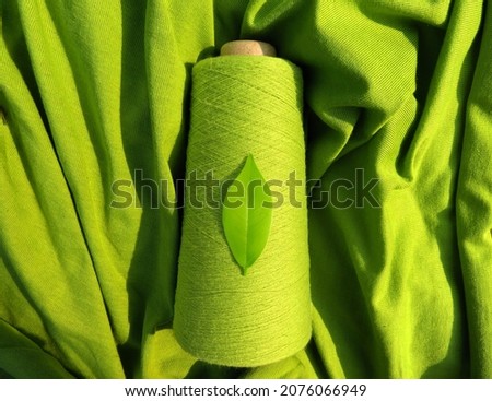 GreenSustainable Fashion:  Leaf on a green yarn cone with a backdrop of a green fabric, symbolising sustainability       